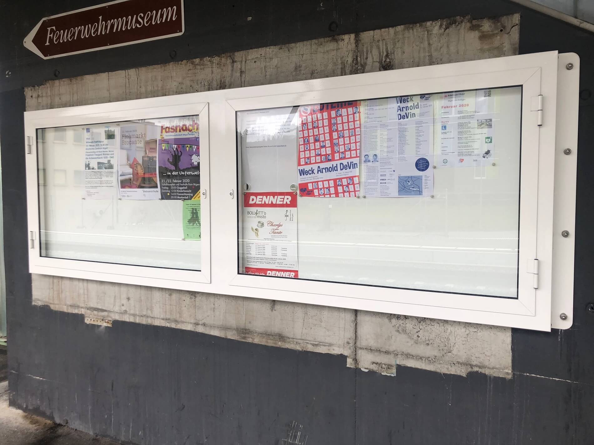 Eine Ankündigungstafel mit mehreren bunten Plakaten und einem Hinweisschild zum Feuerwehrmuseum