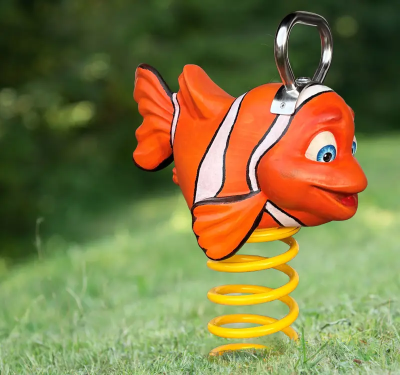 Federwippe in Form eines orangefarbenen Fisches mit weißen Streifen auf einer grünen Wiese