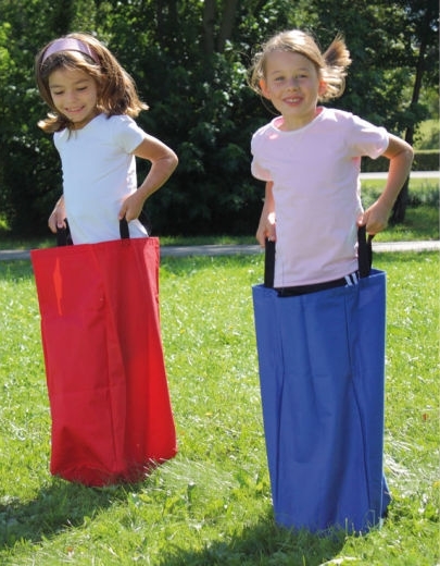 Zwei Kinder spielen im Freien mit roten und blauen Hüpfsäcken auf einer Wiese