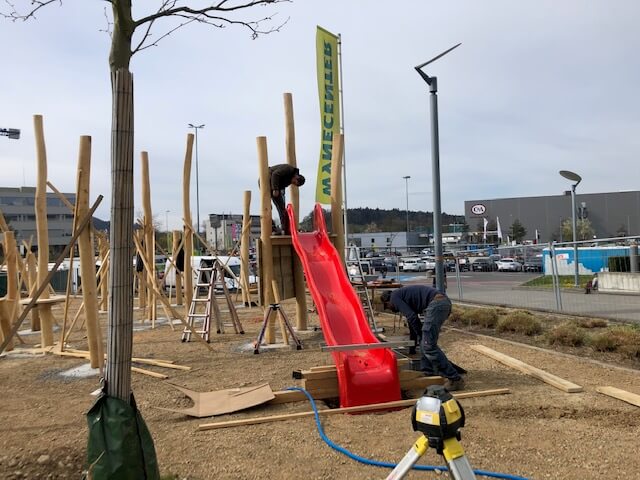 Bau eines Spielplatzes mit Holzstrukturen und roter Rutsche, Arbeiter bei der Montage