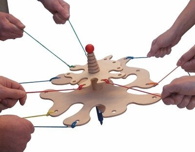 Mehrere Hände halten bunte Seile, die an einem hölzernen Kooperationsspiel befestigt sind, ideal für Teamübungen