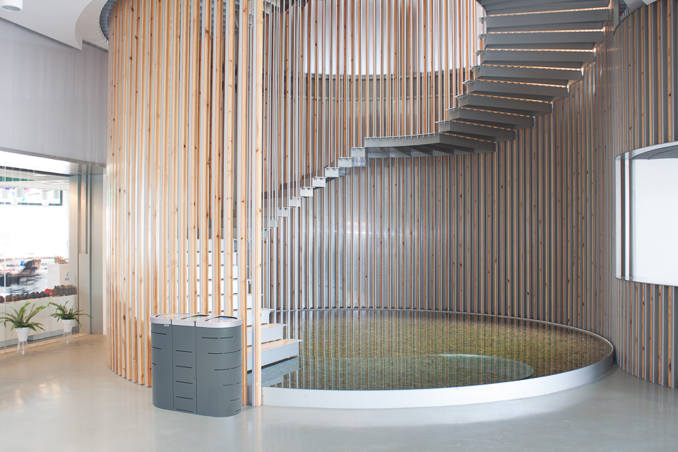 Ein modernes Interieur mit einer eleganten, hölzernen Wendeltreppe, umgeben von vertikalen Holzlatten, führt zu einem oberen Stockwerk, mit darunter liegendem Wasserelement.