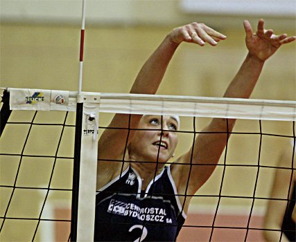 Eine Volleyballspielerin in der Luft, die einen Ball am Netz blockt, mit konzentriertem Gesichtsausdruck.