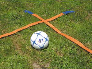 Ein Fußball auf einer grünen Wiese, umgeben von orangenen Markierbändern.