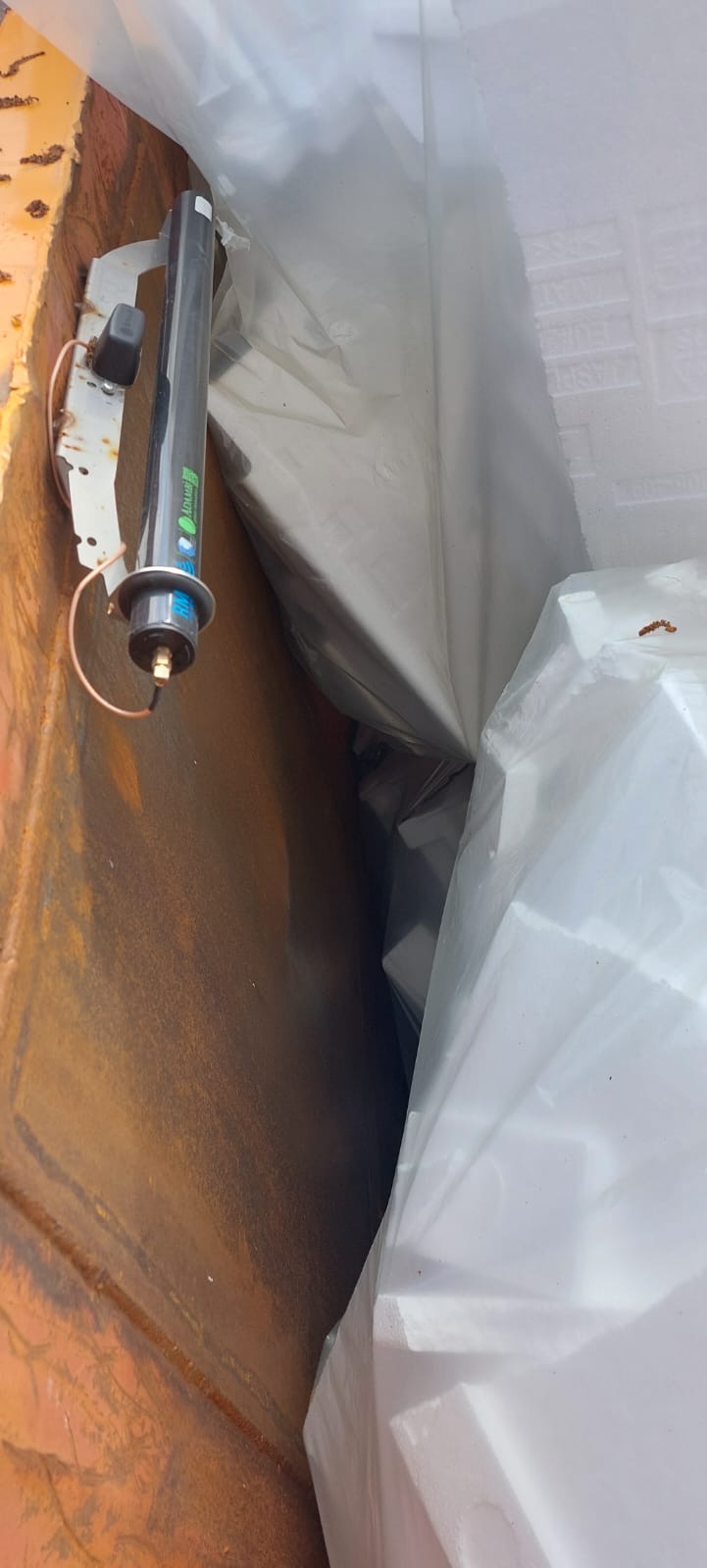 Ein elektrisches Bauteil, montiert an einer rostigen Metalloberfläche, teilweise bedeckt mit einer weißen Kunststofffolie