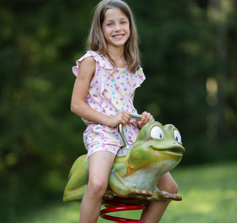 Lächelndes Mädchen sitzt auf einem Froschspielzeug auf dem Spielplatz