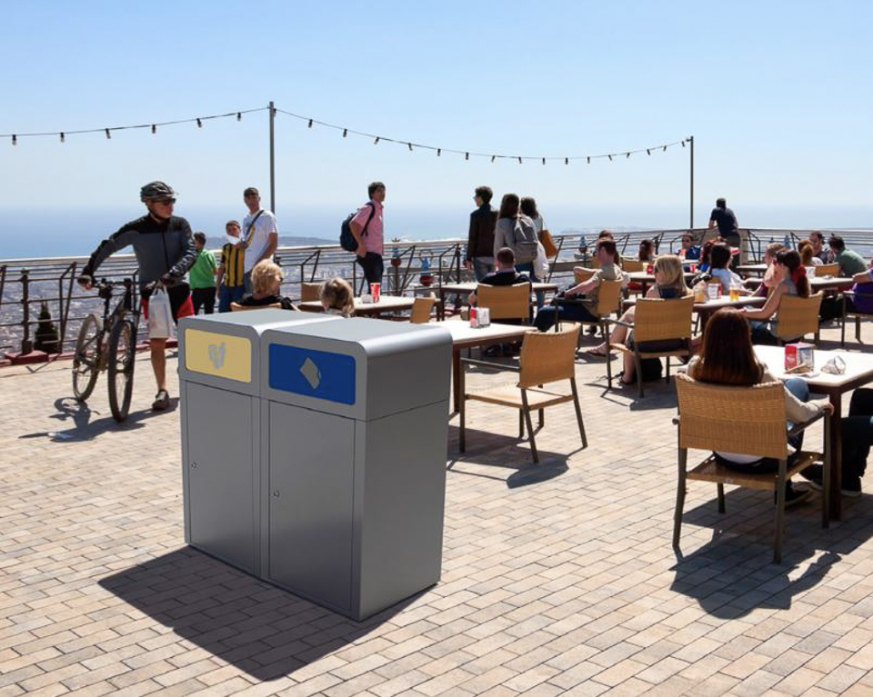 Menschen auf einer sonnigen Terrasse eines Cafés mit originellen Mülleimern und Meerblick