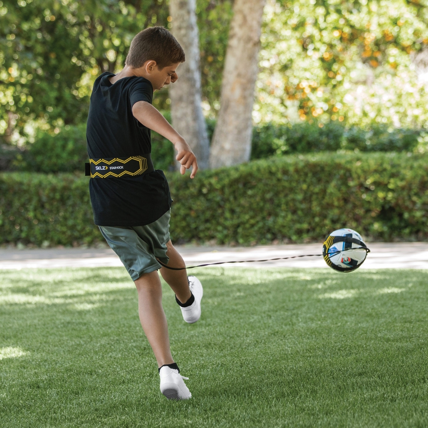 Ein Junge spielt im Garten mit einem Fußball, der an einem Trainingsgurt befestigt ist.