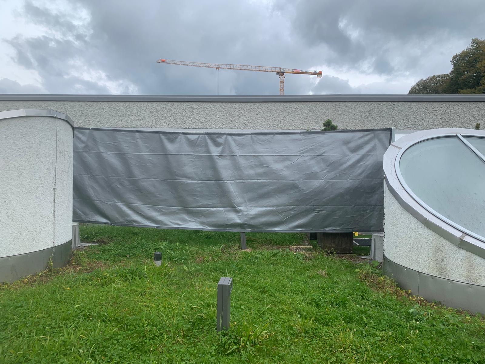 Graue Abdeckplane auf einer Baustelle mit Kran im Hintergrund und bewölktem Himmel