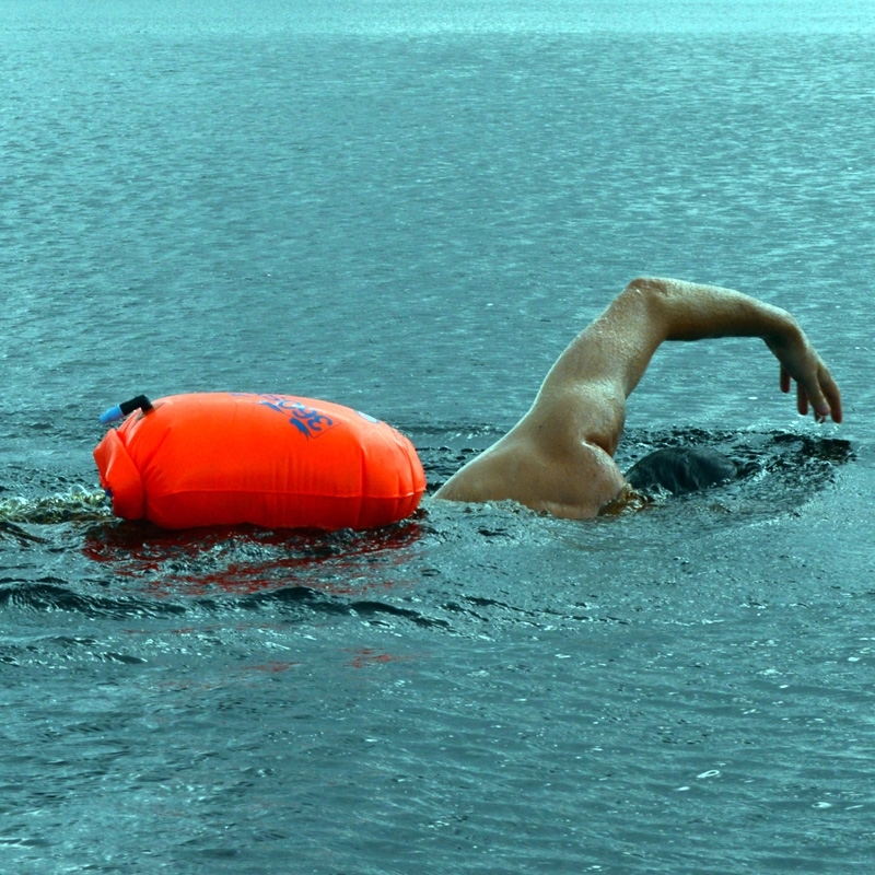 Ein Schwimmer mit einer auffällig orangen Boje schwimmt im offenen Wasser, um für zusätzliche Sichtbarkeit und Sicherheit zu sorgen.