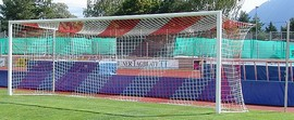 Großes Fußballtor auf einem Sportplatz mit grünem Rasen und bunter Tribüne im Hintergrund