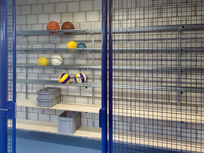Ein offener Ballschrank mit Metallgittern, Holzböden und verschiedenen Sportbällen sowie Aufbewahrungsboxen.