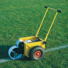 Gelber Linienmarkierungswagen steht auf einem Sportplatz und zieht eine weiße Linie auf das grüne Gras.