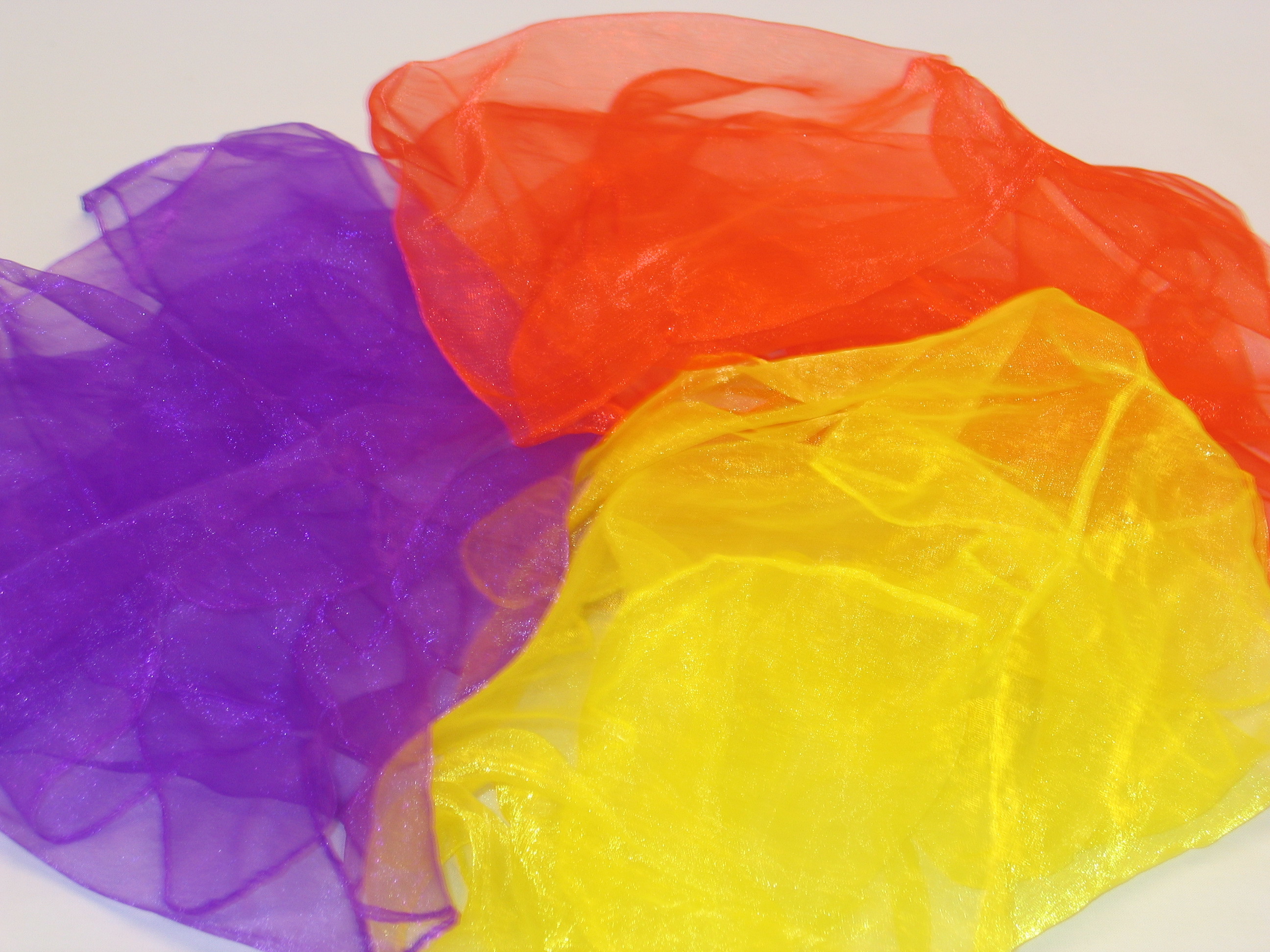 Drei transparente Schals in den Farben Rot, Gelb und Lila auf weißem Hintergrund