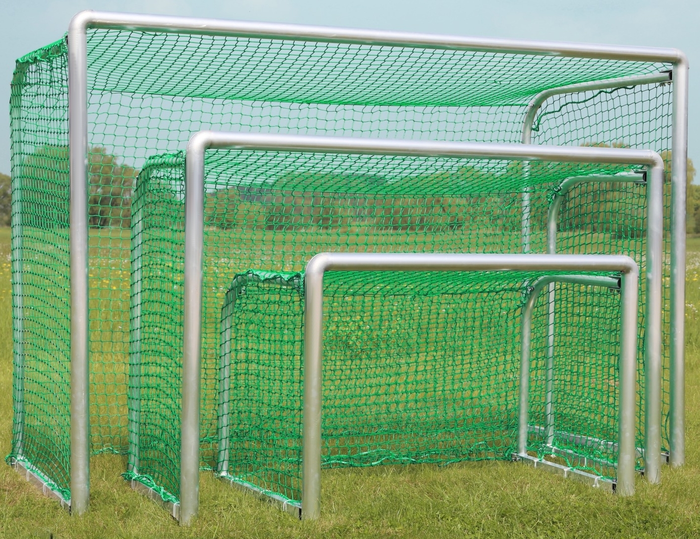 Drei Fußballtore in verschiedenen Größen nebeneinander auf einer Wiese mit grünem Netz
