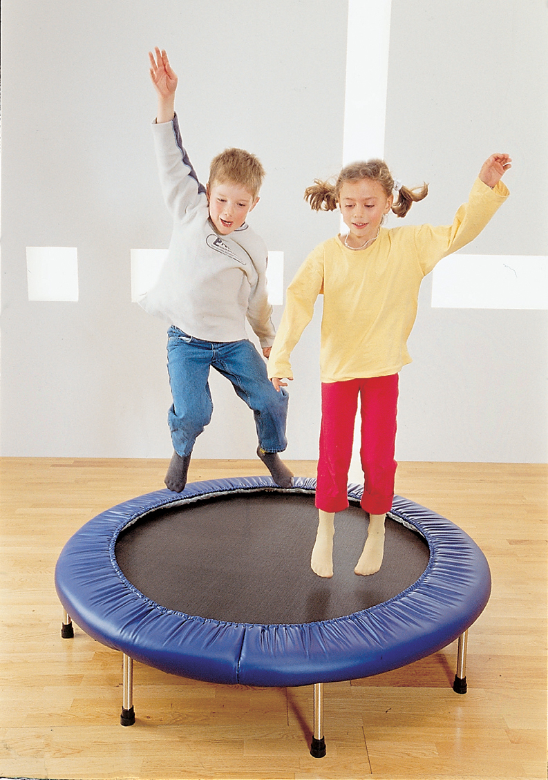 Zwei Kinder, ein Junge und ein Mädchen, genießen das Springen auf einem blauen Mini-Trampolin in einem hellen Raum.