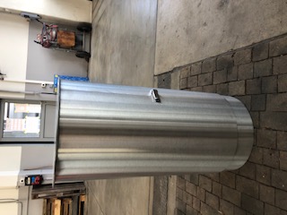 Ein großer, zylindrischer Aluminiumbehälter steht auf einem gepflasterten Boden in einer Lagerhalle.