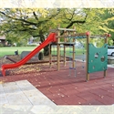 Spielplatz mit roter Rutsche, Klettergerüst und herbstlichem Laub im Hintergrund