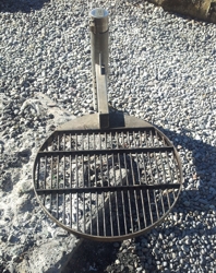 Ein runder Metallgrill mit Rost auf einem Kiesboden platziert, ideal für Outdoor-Camping und Picknick.
