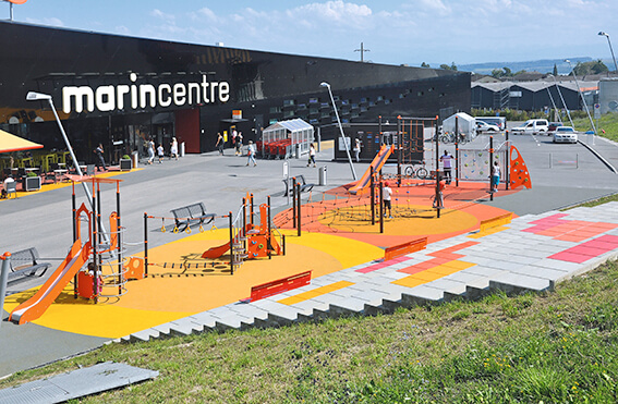 Moderner Spielplatz mit verschiedenen Geräten vor einem Einkaufszentrum bei Tag