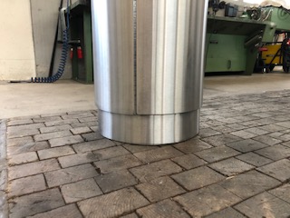 Ein großer, zylindrischer Leichtmetallbehälter steht in einer Werkstatt auf einem gepflasterten Boden. Im Hintergrund sind Maschinen zu sehen.