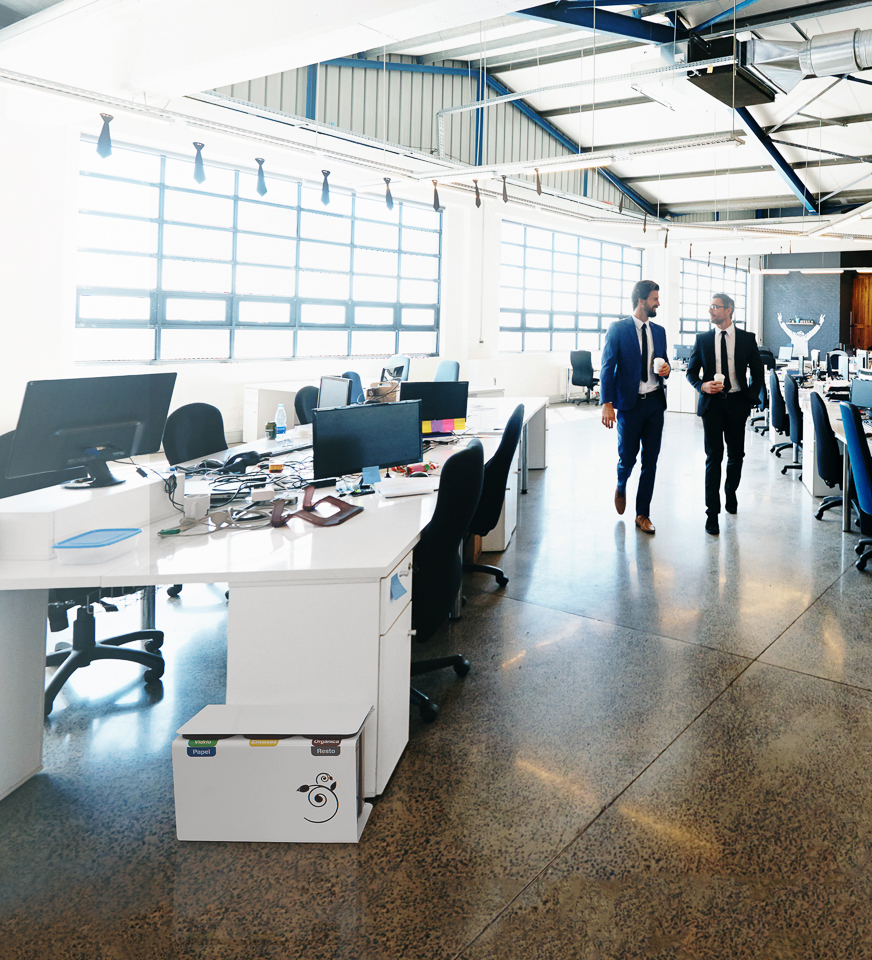 Zwei Männer im Anzug gehen durch ein modernes, sonnendurchflutetes Büro mit offenen Arbeitsplätzen.
